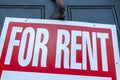 A large For Rent sign white text on red background is attached to  metal door handle on the front door Royalty Free Stock Photo