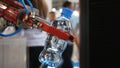 Large robotic hand holding and relocating a bottle with water with people on the background. Media. Different working