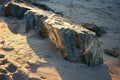 A large rock rests on the sandy beach, contrasting against the smooth texture of the sand, A rocky outcrop jutting out of the sand