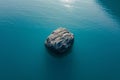 A large rock stands alone in the center of a vast body of water, surrounded by ripples and reflections, Single isolated rock in a Royalty Free Stock Photo