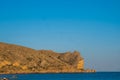 A large rocky promontory rises above the blue sea Royalty Free Stock Photo