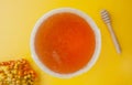 Large round honey bowl , rowan and sea buckthorn berries, honey stick on a yellow background, top view