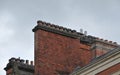 Large row of old fashioned traditional clay chimney pots on a red brick support against a grey sky from when buildings where Royalty Free Stock Photo