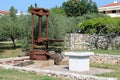 Large rusted metal vintage retro olive oil press machine mounted on concrete foundation next to newly built well used as garden Royalty Free Stock Photo