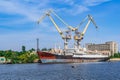 A large rusty abandoned ship against the background of two port cranes