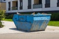 Large rusty blue dumpster container placed near modern apartment building on sunny day Royalty Free Stock Photo