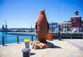 Large rusty penguin statue standing next to the bridge crossing at the Waterfront. Harbor and blue sky in background.