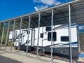 Large RV recreational vehicle under a carport with satellite dish on top. Temporary extended living setup. Toy hauler style