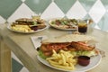 Large sandwich of breaded beef steaks garnished with French fries, sliced tomatoes, dips, glasses with drinks and more background Royalty Free Stock Photo