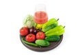 A large selection of vegetables and a Glass of freshly squeezed vegetable juice on a round tray on a white background.