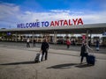 Large signboard Welcome to Antalya at Airport. Tourists with suitcases in the square outside