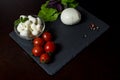 Large and small balls of mozzarella cheese on a stone plate with basil leaves, lettuce, tomatoes and hot pepper Royalty Free Stock Photo