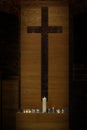 Large and small burning candles in front of a modern simple cross cut out of a wooden plate in the historic St. Georgen church in