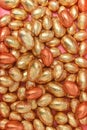 Pile or group of gold, orange and bronze foil wrapped chocolate easter eggs, against a peach orange background