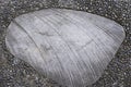 Smooth gray stone with lines on a gravel pavement and dirt