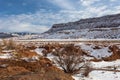 Large snow covered field with red dirt and rocks in front of a large mesa plateau in rural New Mexico