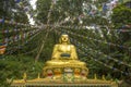 A large statue of a golden sitting Buddha in a green forest and multicolored prayer flags of Tibet above him Royalty Free Stock Photo