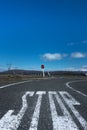 Large `stop` lettering painted on tarmac road & red sign post viewed from low level with blue sky, clouds & snow capped mountain