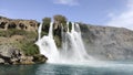 A large strong waterfall falls from a rocky precipitous shore into the blue Mediterranean Sea