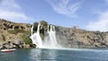 A large strong waterfall falls from a rocky precipitous shore into the blue Mediterranean Sea