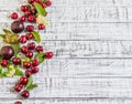 Large sweet juicy cherries, plums and grapes, foliage and flowers on a wooden background