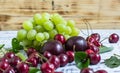 Large sweet juicy cherries, plums and grapes, foliage and flowers on a wooden background