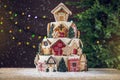 Large tiered Christmas cake decorated with gingerbread cookies and a house on top. Tree and garlands in the background.