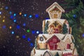 Large tiered Christmas cake decorated with gingerbread cookies and a house on top. Tree and garlands in the background.