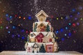 Large tiered Christmas cake decorated with gingerbread cookies and a house on top. Tree and garlands in the background. Royalty Free Stock Photo