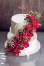 A large tiered wedding cake decorated with red roses on the table