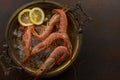 Large Tiger shrimps with lemon and ice cubes on ancient plate on dark stone background. Top view on appetizing seafood snack