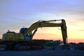 Large tracked excavator with with hydraulic hammer breaks asphalt at a construction site against on the background sunset. Royalty Free Stock Photo