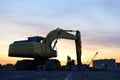 Large tracked excavator with with hydraulic hammer breaks asphalt at a construction site against on the background sunset. Royalty Free Stock Photo