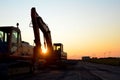 Large tracked excavator with with hydraulic hammer breaks asphalt at a construction site against on the background sunset. Royalty Free Stock Photo