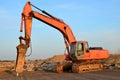 Large tracked excavator with with hydraulic hammer breaks asphalt at a construction site against on the background sunset. Road Royalty Free Stock Photo