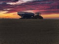 Large tractor pulling a tracked grain cart loaded with corn at sunset