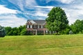 Large traditional red brick colonial house with fluffy wood. Green lawn and blue sky Royalty Free Stock Photo