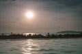 Large tropical Sun in hazy sky - view over roof top swimming pool in luxury hotel. Palms, sea and mountains at horizon line.