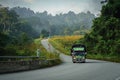 Large truck driving down a peaceful and picturesque rural road with a line of lush green trees