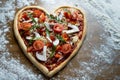 A large vegetable pizza in the shape of a heart lies on a wooden table.