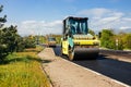 Large vibratory roller compact fresh asphalt on the road surface of a new construction site