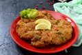 Large Viennese schnitzel on a red plate with lemon on a black background.