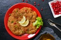 Large Viennese schnitzel on a red plate with lemon on a black background. Meat dish.