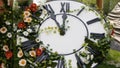 Large wall clock on the field in blooming flowers, showing the time 11:55, 12:00. time management concept, daylight Royalty Free Stock Photo