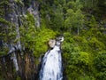 A large waterfall in the back of the Altai Mountains with gray-brown stones near a steep cliff with green trees. Waterfalls Korbu