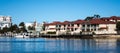 Large waterside houses, apartment condominiums in suburban community on riverfront with boat moored at wharf, blue sky in backgrou