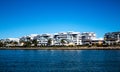 Large waterside houses built in front of condominium apartments with riverside grass frontage, stone retaining wall and blue river Royalty Free Stock Photo