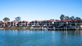 Large waterside houses in suburban community set on riverfront with wooden wharf and boat in foreground, blue sky in background