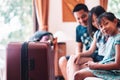 Large wheeled suitcase standing on the floor in the hotel room with happy asian family sitting on the bed in background