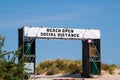 Large white banner over entrance to a beach that says, Beach Open Social Distance